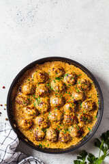 Swedish meatballs in creamy sauce in black frying pan, gray background. Scandinavian food concept.