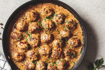 Swedish meatballs in creamy sauce in black frying pan, gray background. Scandinavian food concept.