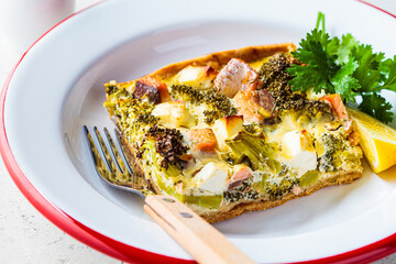 Piece of quiche pie with salmon and broccoli in plate.
