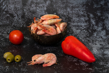 fresh peppers, tomato, olives and frozen prawns in an eco-friendly coconut bowl on a dark background