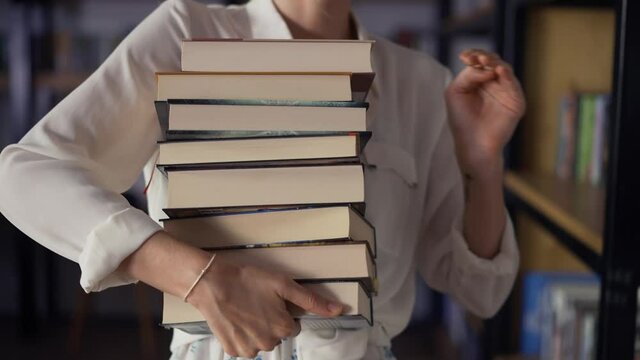 Woman holding pile of books in the library, putting more on the stack