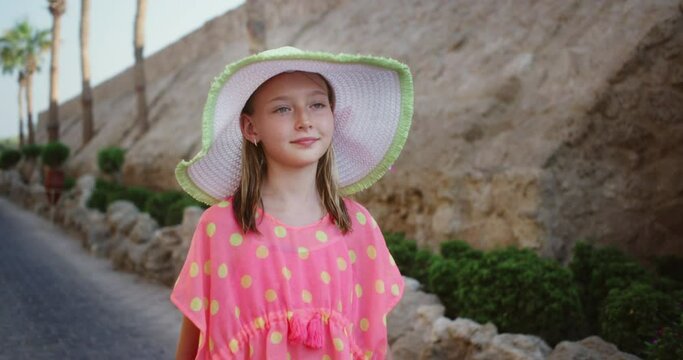 Portrait happy teenager girl in summer hat walking on street resort hotel. Beautiful young woman in straw hat walking at summer street while resting in resort
