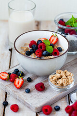 Bowl with vegan granola with fresh ripe organic berries, plant milk, mint. Concept of dieting, detox, tasty simple super food, healthy low calories breakfast. Wooden background, close up