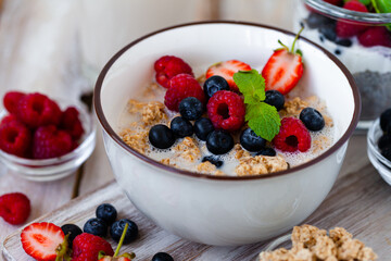 Bowl with vegan granola with fresh ripe organic berries, plant milk, mint. Concept of dieting, detox, tasty simple super food, healthy low calories breakfast. Wooden background, close up