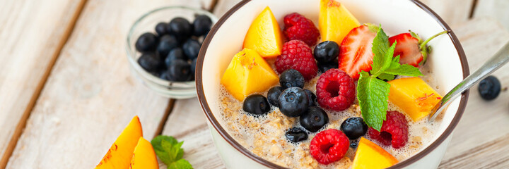 Bowl with vegan granola with fresh ripe organic berries, peach, plant milk, mint. Concept of dieting, detox, tasty simple super food, healthy low calories breakfast. Wooden background, close up banner