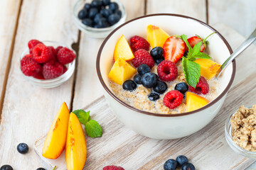 Bowl with vegan granola with fresh ripe organic berries, peach, plant milk, mint. Concept of dieting, detox, tasty simple super food, healthy low calories breakfast. Wooden background, close up