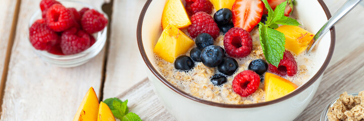 Bowl with vegan granola with fresh ripe organic berries, peach, plant milk, mint. Concept of dieting, detox, tasty simple super food, healthy low calories breakfast. Wooden background, close up banner