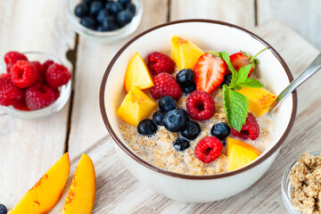 Bowl with vegan granola with fresh ripe organic berries, peach, plant milk, mint. Concept of dieting, detox, tasty simple super food, healthy low calories breakfast. Wooden background, close up