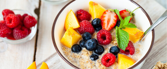 Bowl with vegan granola with fresh ripe organic berries, peach, plant milk, mint. Concept of dieting, detox, tasty simple super food, healthy low calories breakfast. Wooden background, close up banner
