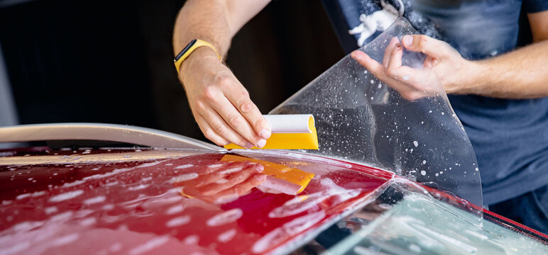 Master man installs strip of vinyl film in risk zone of windshield to protect car body paint from scratches and chips