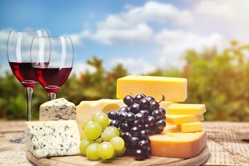 Beautiful glasses of wine and a wooden plate with cheese served outside.