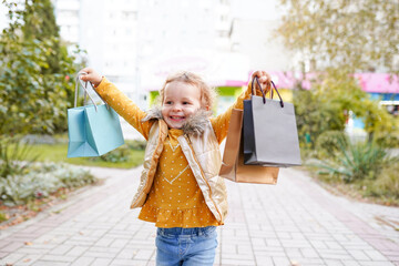 Child girl in autumn orange cloth with shopping bags outdoors