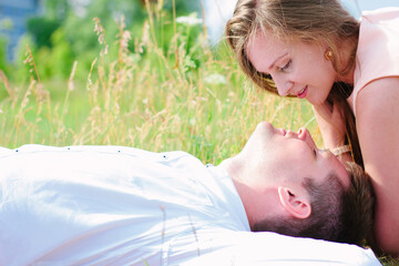 Girl and man couple laying down on a lawn and look to each others eyes