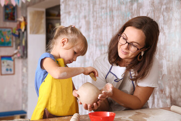 Mother and kid daughter molded from clay at pottery class
