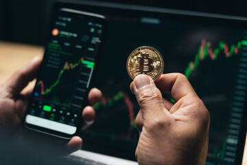 Businessman holding golden bitcoin on computer trading chart screen background. stock, cryptocurrency trading Concept.... © Suriyawut