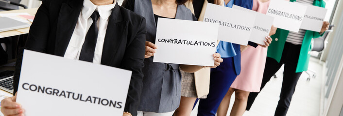 Businesspeople group in business clothes set row and holding paper banner with word congratulations and show to camera. Concept of greeting and appreciation for success in job or work in company