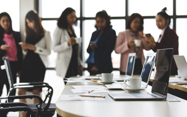Selective focus on working desk, group of unrecognizable businesswomen standing together in office at breaking time. Female employee teamwork taking with relax in blur background