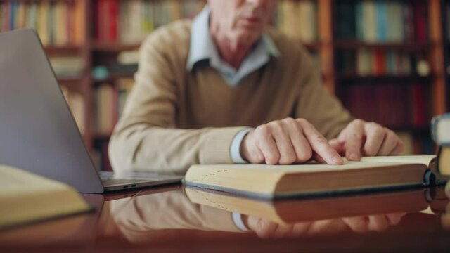 Senior historian reading a book and typing notes on laptop, working on article