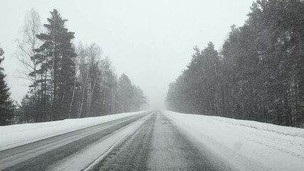 View through the windshield of a car on an empty snowy and icy road in winter in heavy snowfall with poor visibility in the forest. - Powered by Adobe