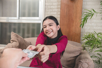 A young woman happily receives her allowance in cash from her father while sitting on a sofa at the living room. A teenager of mixed Filipino and European descent.