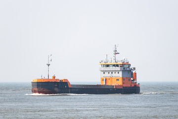 Fototapeta premium Orange and black color cargo sea vessel sails in Baltic sea on foggy day.