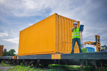 Engineer railway wearing safety uniform holding radio communication on hand for inspection and check container truck railway distribution,there are logistic transportation business.