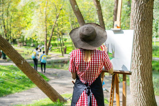 Woman artist wearing big hat at the plein air in the city park.