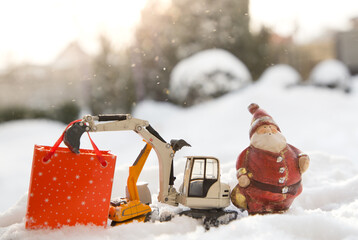 Two models of toy excavators, a souvenir Santa Claus, a gift bag stand in snow. concept for Christmas business greetings, New Year holidays in construction companies. Sunny winter holiday