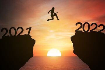 New year concept; pass from 2021 to 2022 , silhouette man jump over barrier cliff and success with...