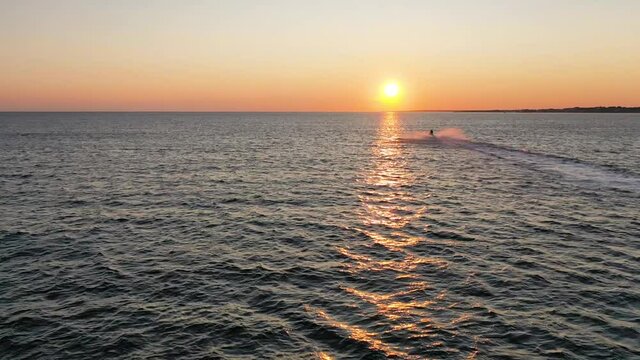 Beautiful sunset on the horizon with water scooter moving away towards the west sun