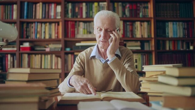 Mature male scientist giving advice over phone referring to information in books