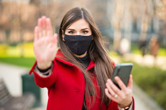 Masked woman showing the stop sign, coronavirus pandemic social isolation, business halt and stay at home