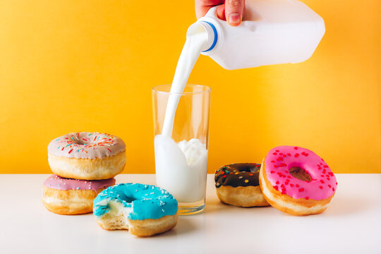 Colorful donuts with sweet jam and peanut butter filling on gray table. Man hand pouring plant milk to the glass. Front view yellow