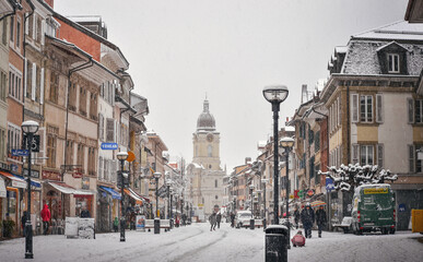Old town main street and church in winter. People walking on the street and kids playing under the snow.