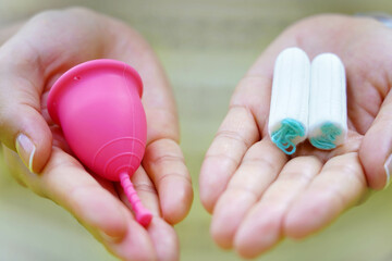 Close-up of woman hands showing collector menstrual cup and tampons