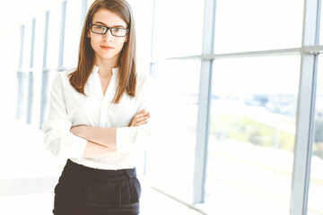 Beautiful female specialist with arms crossed standing in modern office and smiling charmingly. Working on design, data analysis, plan strategy. Business people concept
