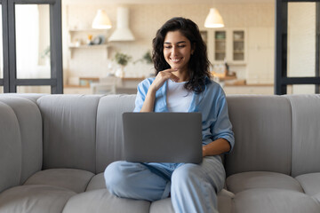 Freelancing, online job or studies. Cheerful young woman sitting on sofa with laptop, working or learning from home