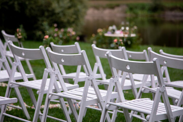 wedding guest chairs for ceremony. Elegant decoration of a wedding ceremony outdoors. Outdoor wedding ceremony with beautiful white furniture.