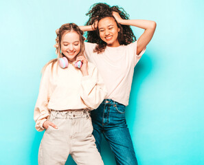 Two young beautiful smiling international hipster female in trendy summer clothes. Sexy carefree women posing near blue wall in studio. Positive models having fun. Concept of friendship
