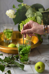 Fresh organic pear mojito lemonade green cocktail with ice on a tile table with flowers of hydrangea and fresh local harvest fruit