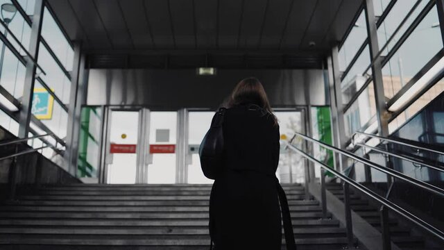 A Girl In A Black Coat Climbs The Stairs At The Exit Of The Subway. Shooting From Behind In Slow Motion