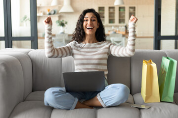 Emotional young lady with laptop and shopping bags buying things online on sale, purchasing goods...