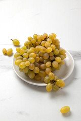 Vertical image of tasty yellow grape on the plate,white kitchen table