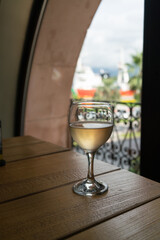 A glass of cold white wine on a hot summer day on a wooden table against the background of an oval window with clouds in the background