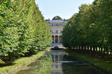 Fototapeta na wymiar A beautiful tree-lined alley that discovers part of a magnificent castle with a pond in foreground. Picture taken in Chantilly, France.