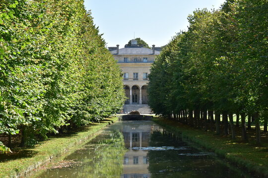 A beautiful tree-lined alley that discovers part of a magnificent castle with a pond in foreground. Picture taken in Chantilly, France.