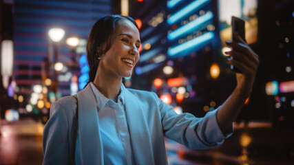 Beautiful Young Woman Using Smartphone for Video Call on Night City Street with Neon Lights....