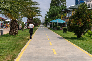 A man in a white t-shirt runs under the green leaves of palm trees on a sunny summer day