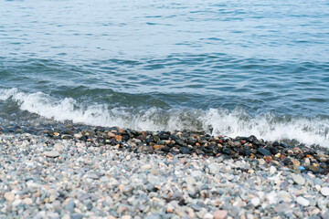 On the edge of the sea beach, the sea wave washes the coastal multi-colored stones on a sunny summer day