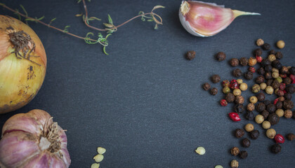 Garlic, onion, rosemary and mix of pepper on black board with copy space. Spices and garlic with yellow onion. Italian cuisine recipe. Healthy food. Cooking concept. Homemade meals. Food ingredients.